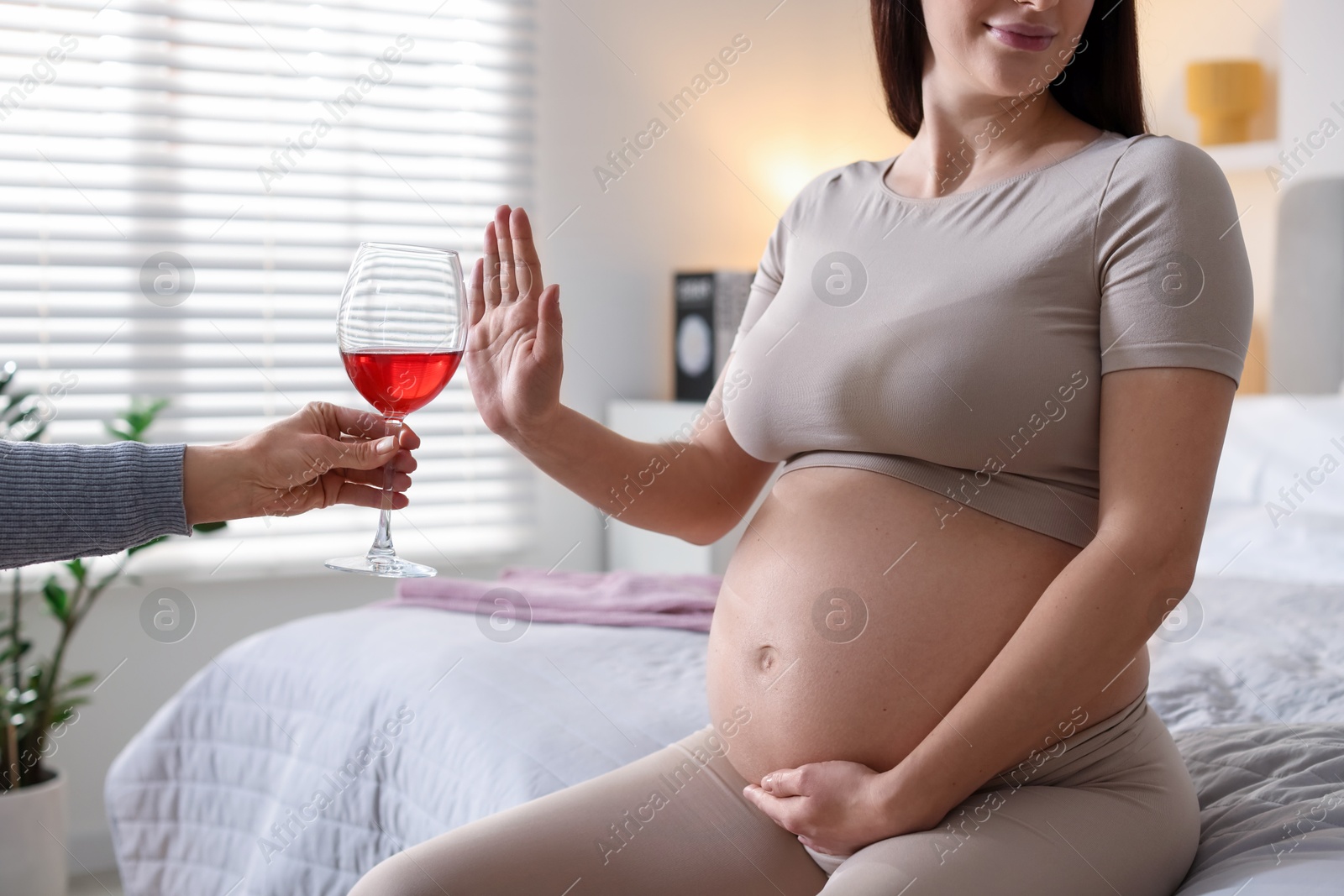 Photo of Pregnant woman refusing glass of red wine at home, closeup