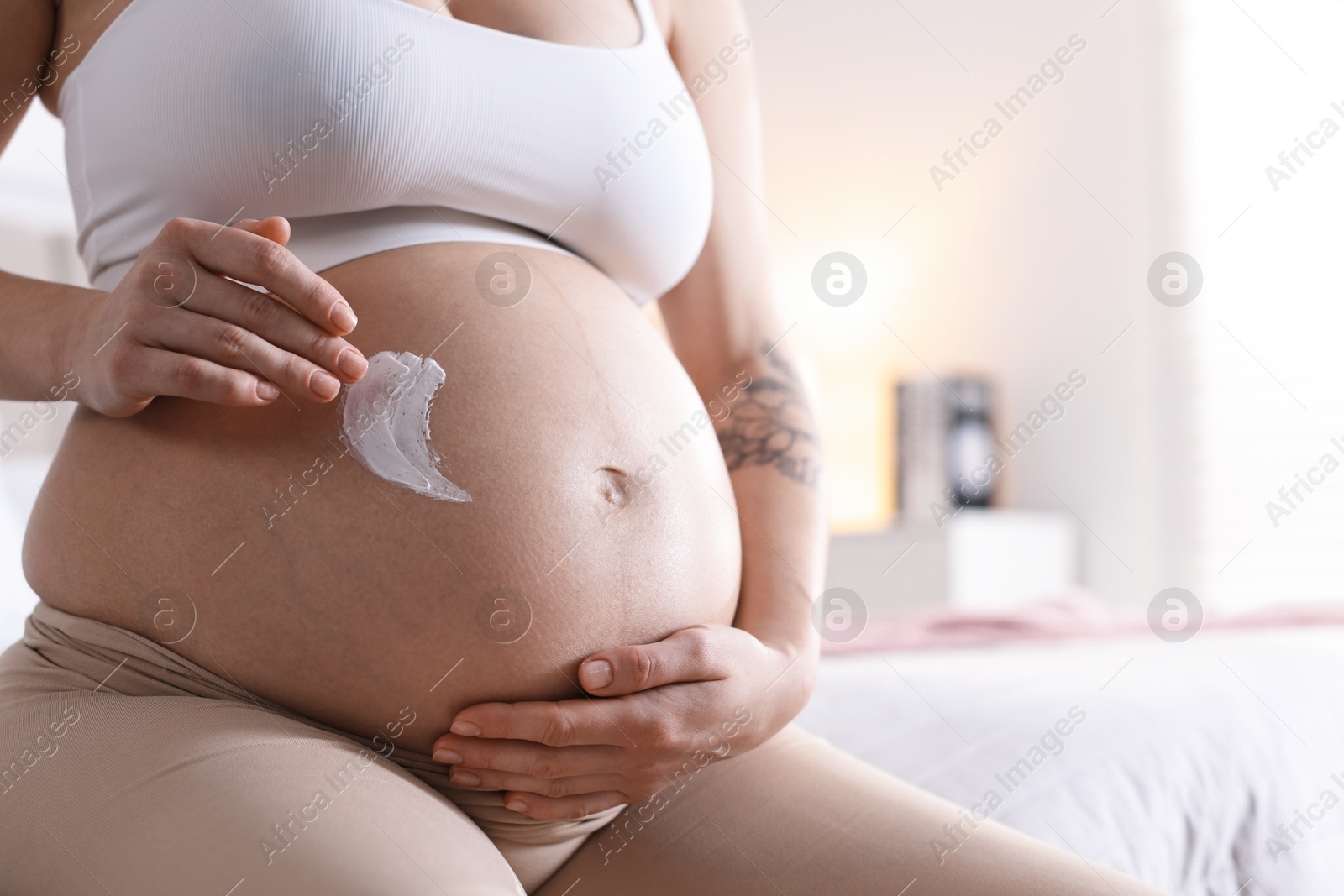 Photo of Pregnant woman applying cream on belly at home, closeup. Space for text