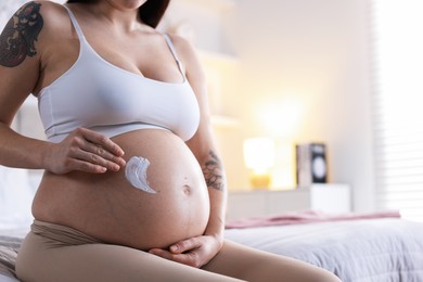 Photo of Pregnant woman applying cream on belly at home, closeup. Space for text