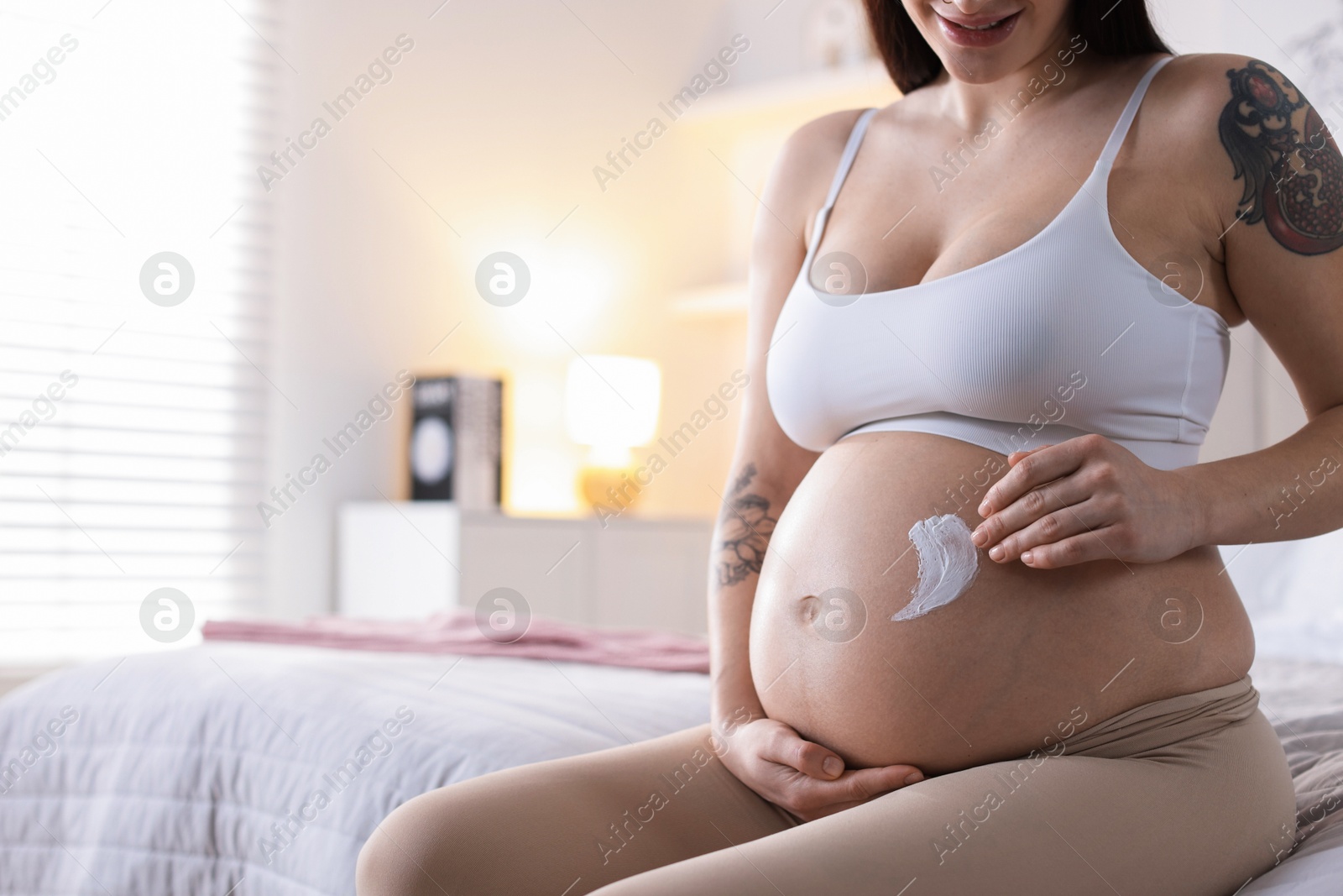 Photo of Pregnant woman applying cream on belly at home, closeup. Space for text