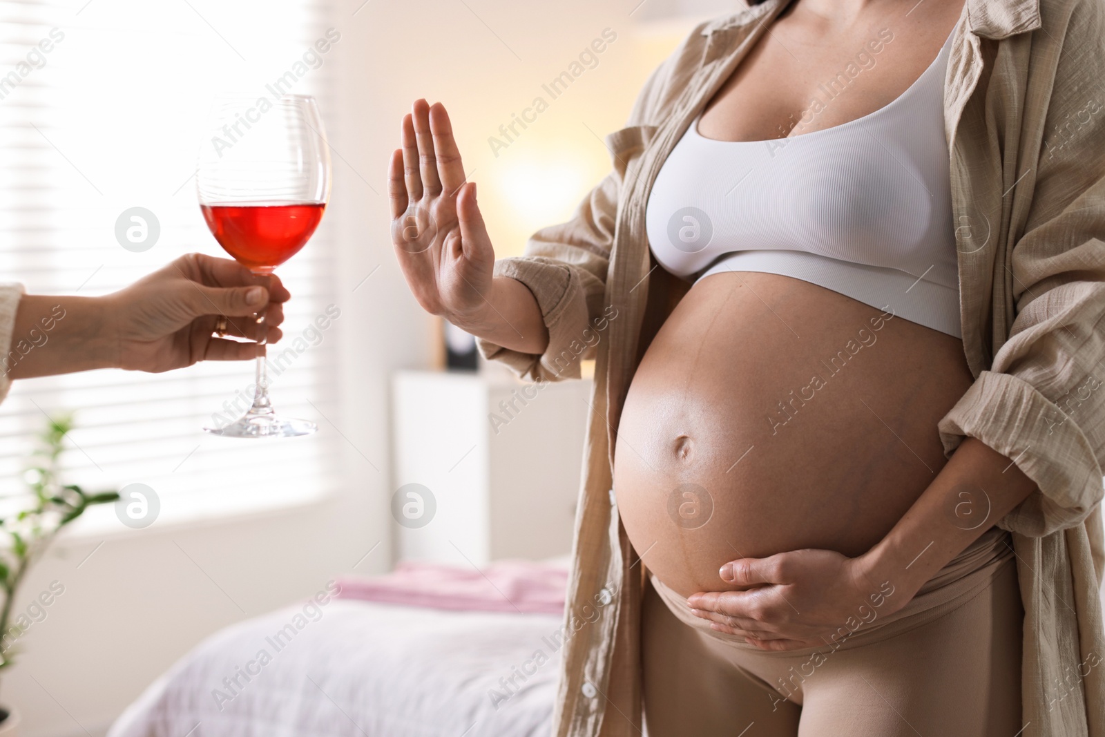 Photo of Pregnant woman refusing glass of red wine at home, closeup