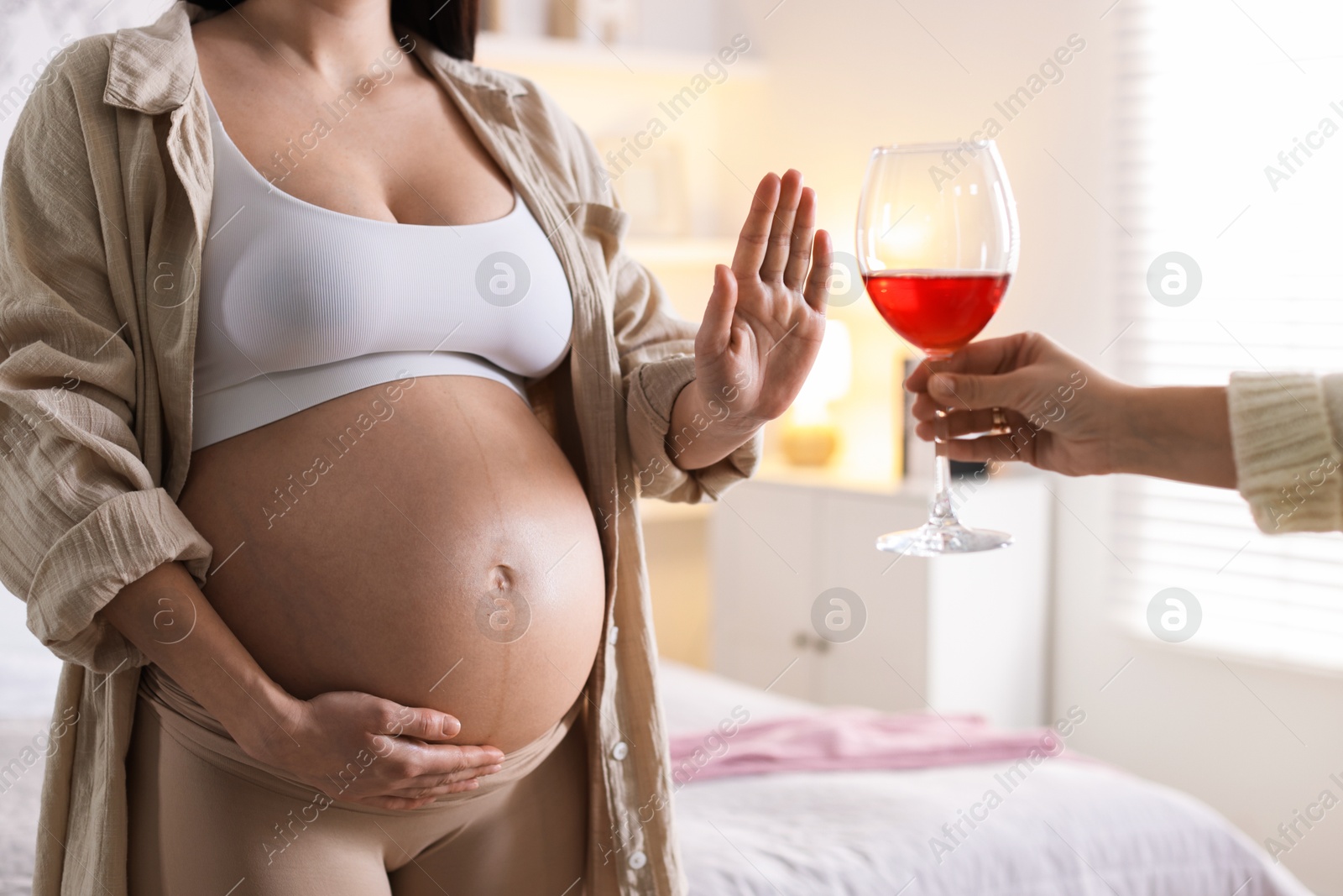 Photo of Pregnant woman refusing glass of red wine at home, closeup