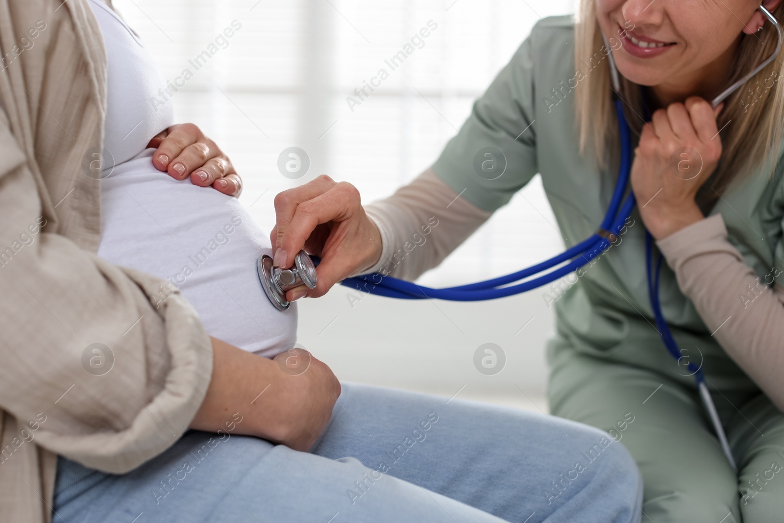 Photo of Pregnancy checkup. Doctor with stethoscope listening baby's heartbeat in patient's tummy indoors, closeup