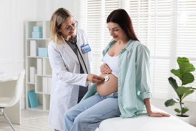 Pregnancy checkup. Doctor with stethoscope listening baby's heartbeat in patient's tummy indoors