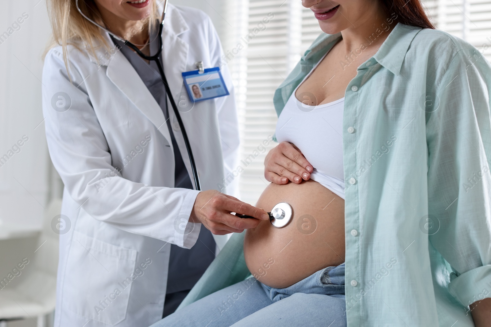 Photo of Pregnancy checkup. Doctor with stethoscope listening baby's heartbeat in patient's tummy indoors, closeup