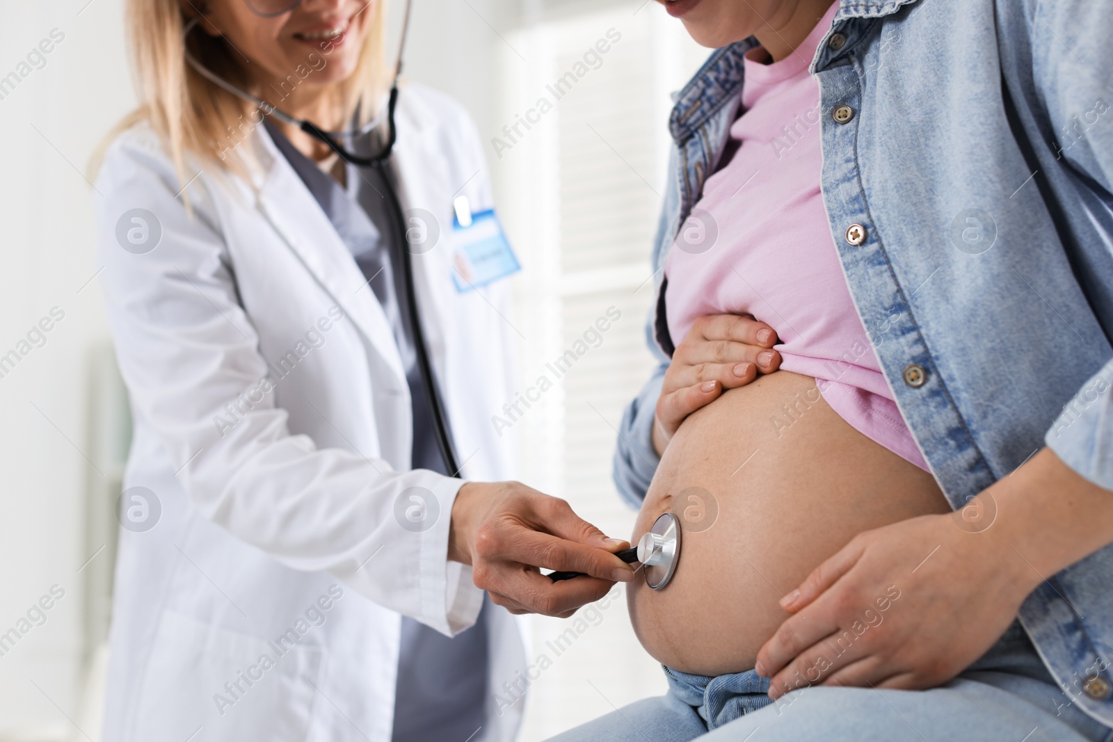 Photo of Pregnancy checkup. Doctor with stethoscope listening baby's heartbeat in patient's tummy indoors, closeup