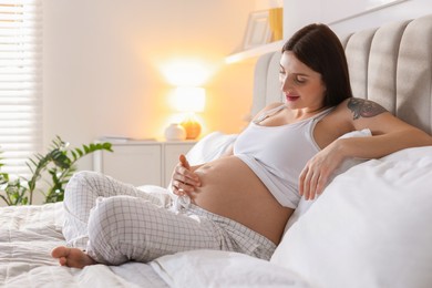 Beautiful pregnant woman with cute belly on bed at home