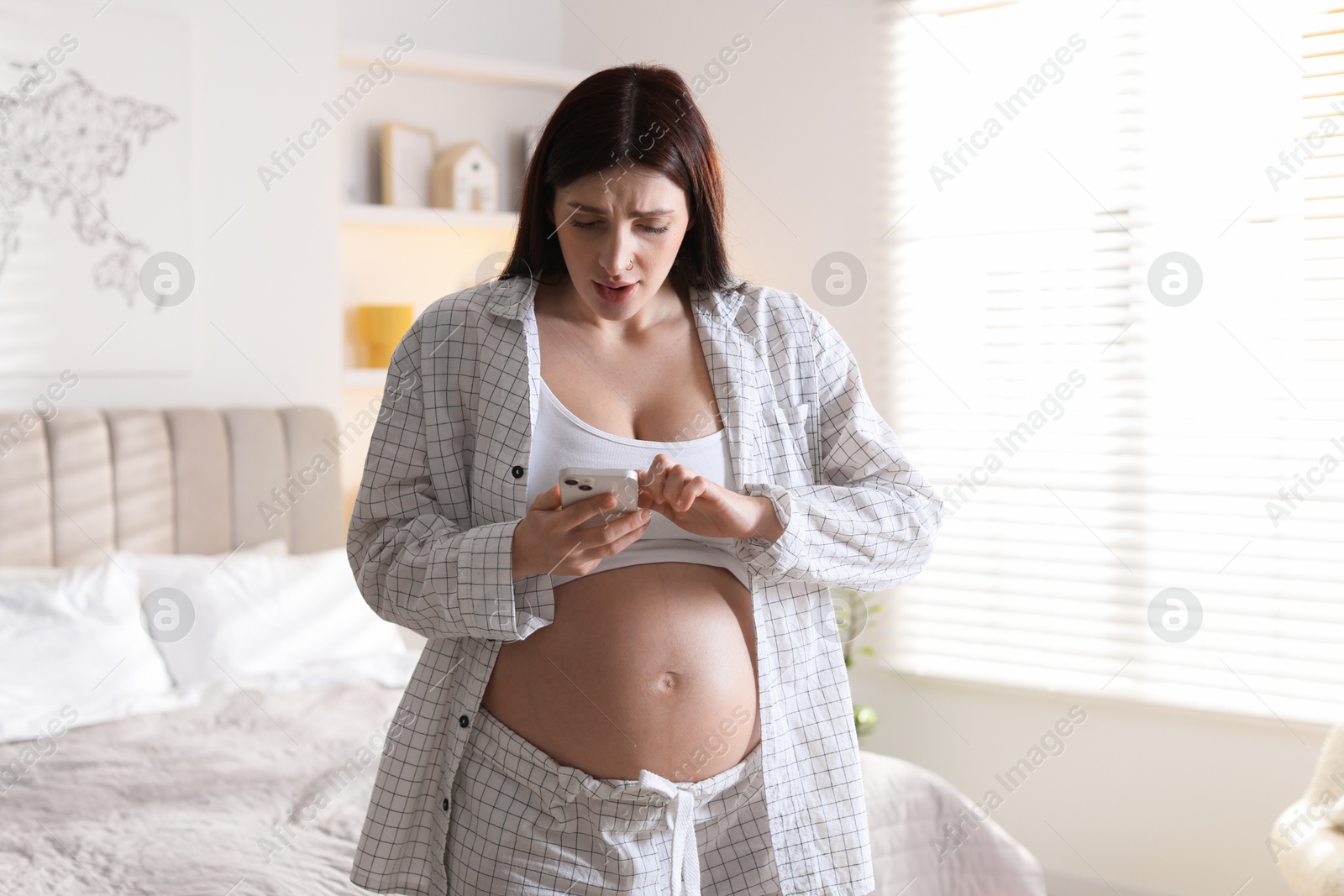 Photo of Beautiful pregnant woman using smartphone at home