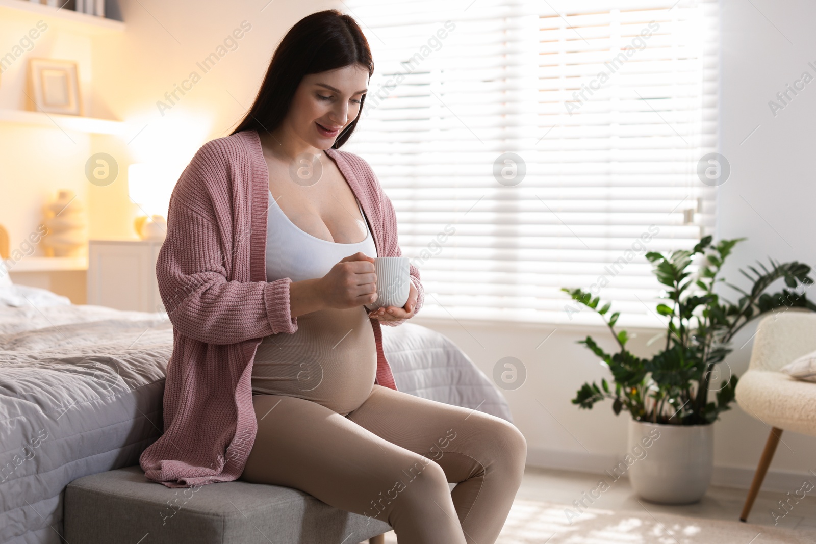 Photo of Beautiful pregnant with cup of drink at home, space for text