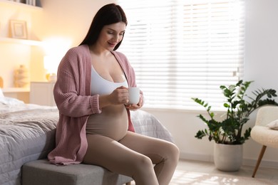 Beautiful pregnant with cup of drink at home, space for text