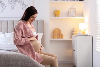 Photo of Beautiful pregnant woman with cute belly on bed at home, space for text