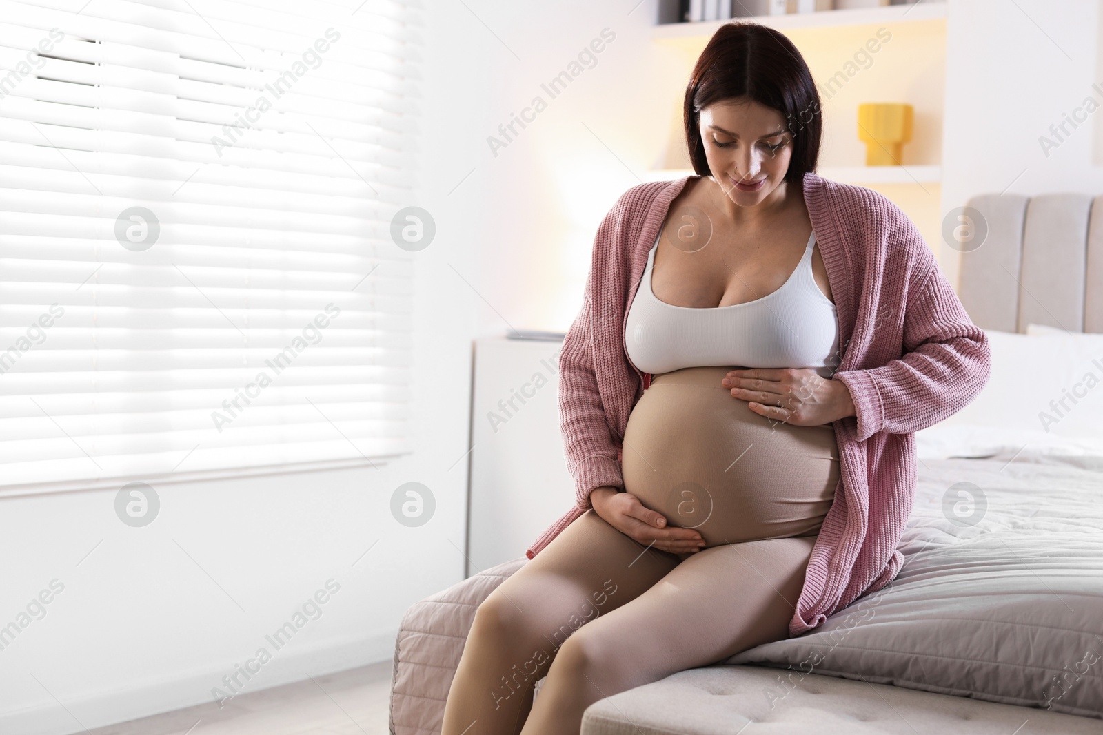 Photo of Beautiful pregnant woman with cute belly on bed at home, space for text