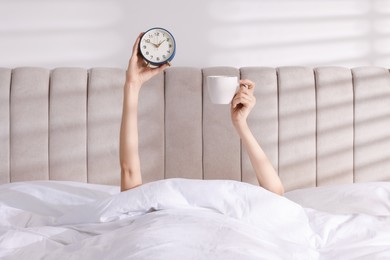 Photo of Woman with alarm clock and cup in bed at home, closeup. Good morning