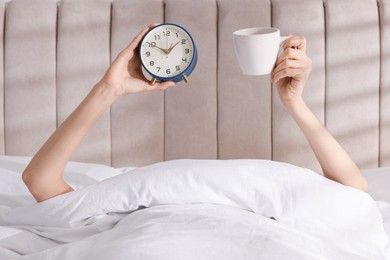 Photo of Woman with alarm clock and cup in bed at home, closeup. Good morning