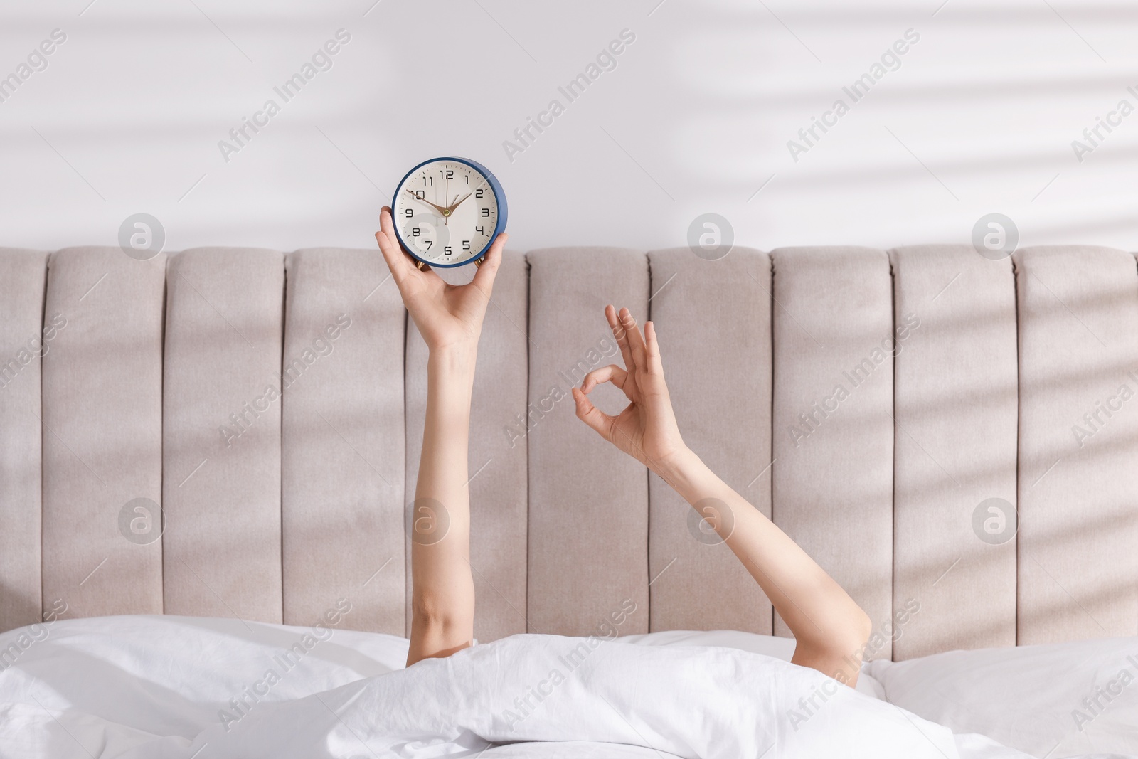 Photo of Woman with alarm clock showing ok gesture in bed at home, closeup. Good morning