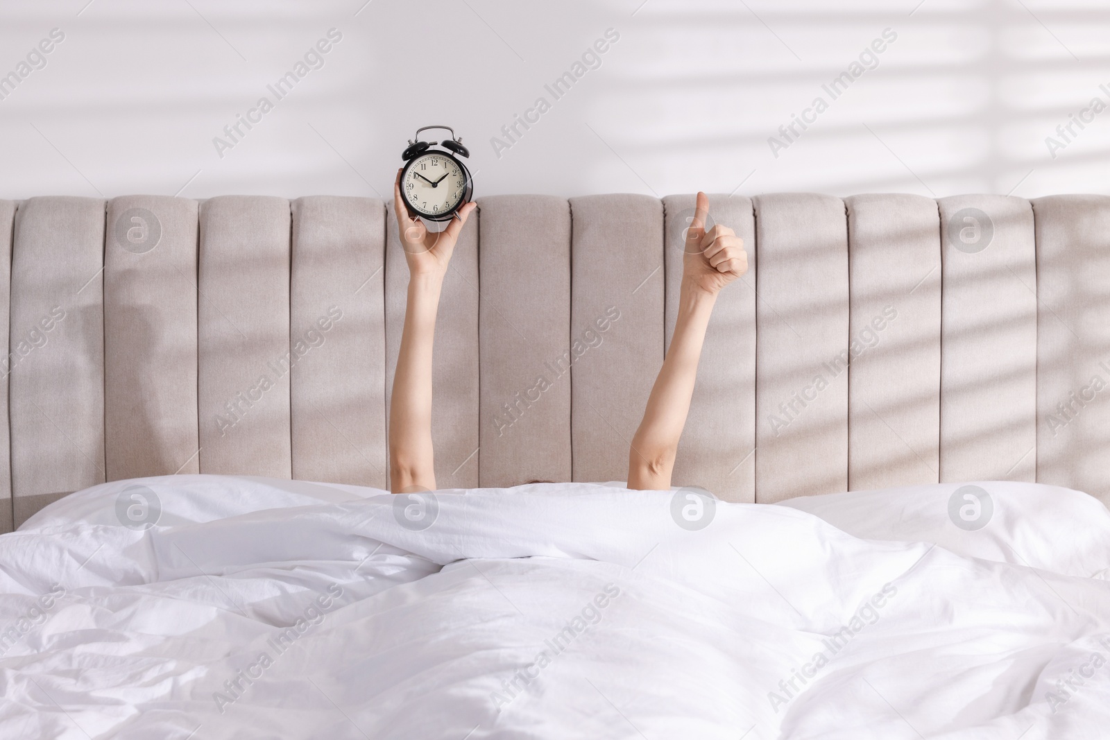 Photo of Woman with alarm clock showing thumbs up in bed at home, closeup. Good morning