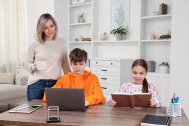 Photo of Smiling mother helping her children with homework at table indoors