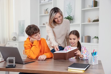 Photo of Smiling mother helping her children with homework at table indoors