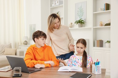 Photo of Mother and her children doing homework at table indoors