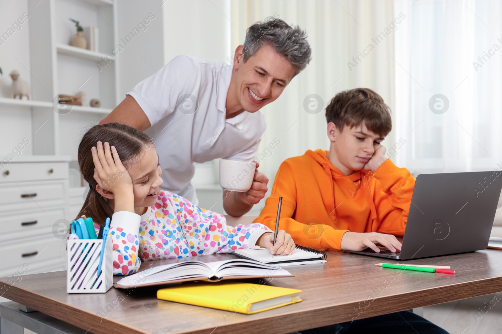 Photo of Smiling father helping his children with homework at table indoors