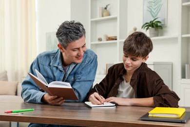 Photo of Smiling father helping his son with homework at table indoors