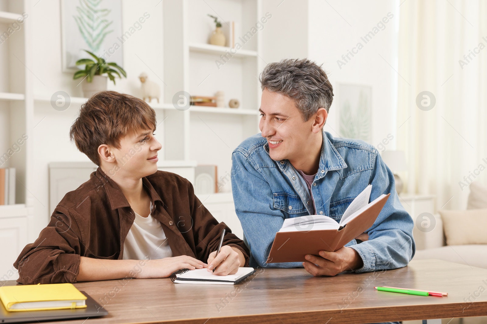 Photo of Smiling father helping his son with homework at table indoors