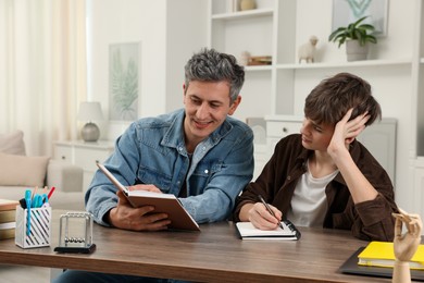 Photo of Smiling father helping his son with homework at table indoors