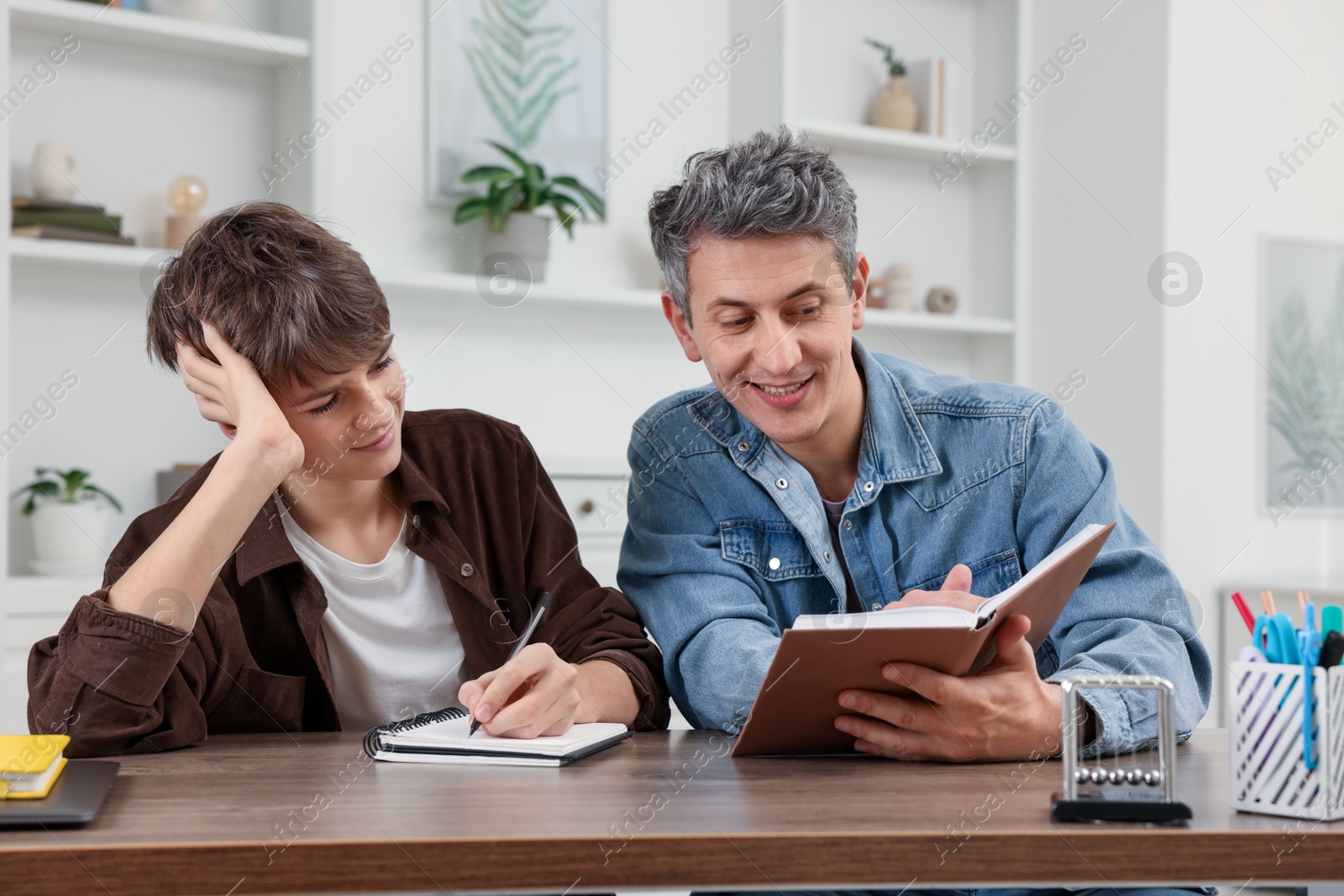 Photo of Smiling father helping his son with homework at table indoors