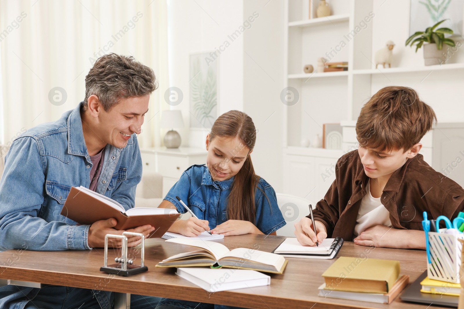 Photo of Smiling father helping his children with homework at table indoors