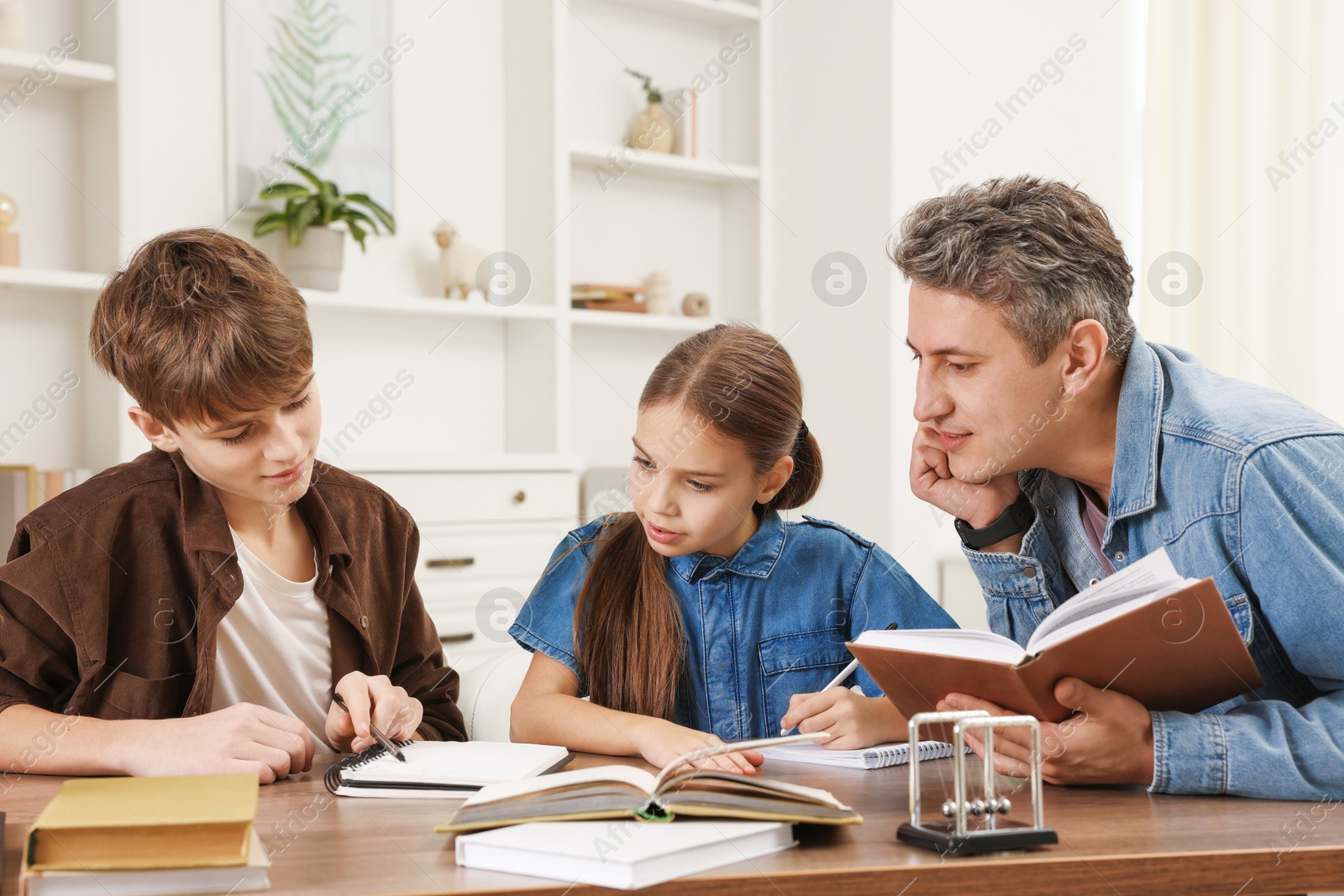 Photo of Father helping his children with homework at table indoors