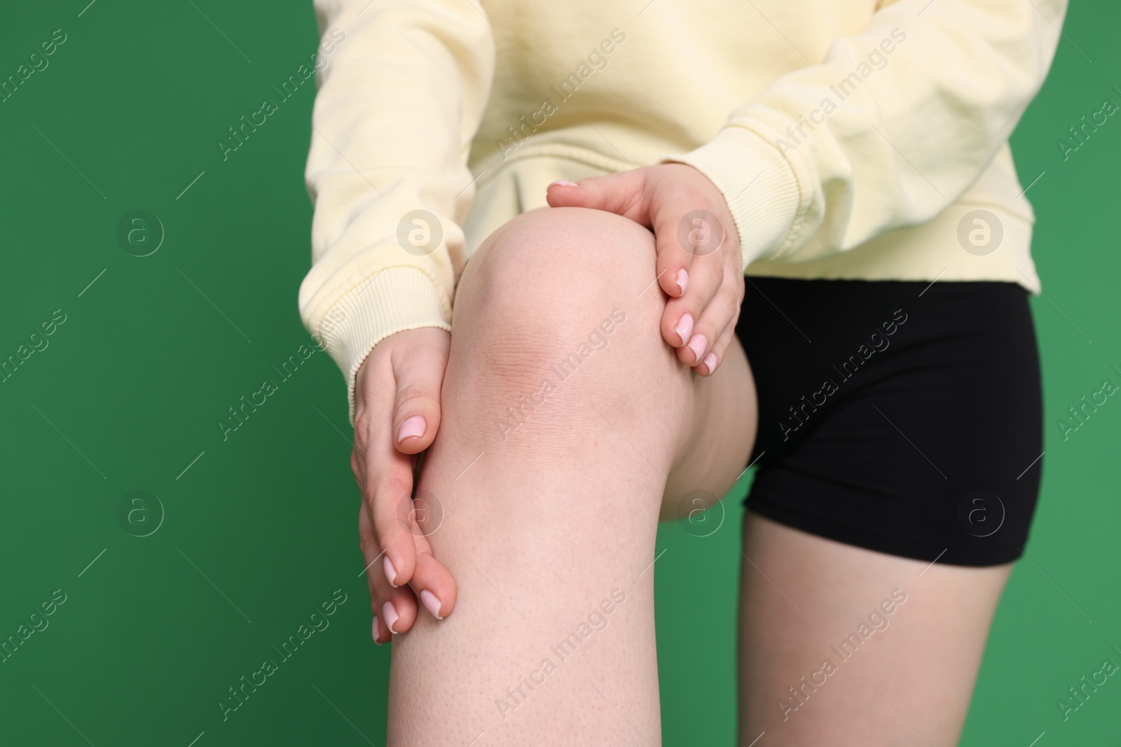 Photo of Young woman suffering from pain in knee on green background, closeup