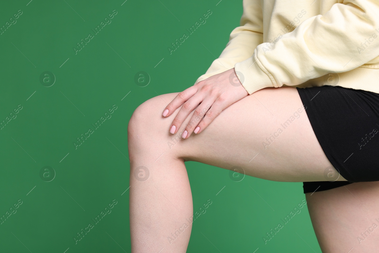 Photo of Young woman suffering from pain in knee on green background, closeup. Space for text