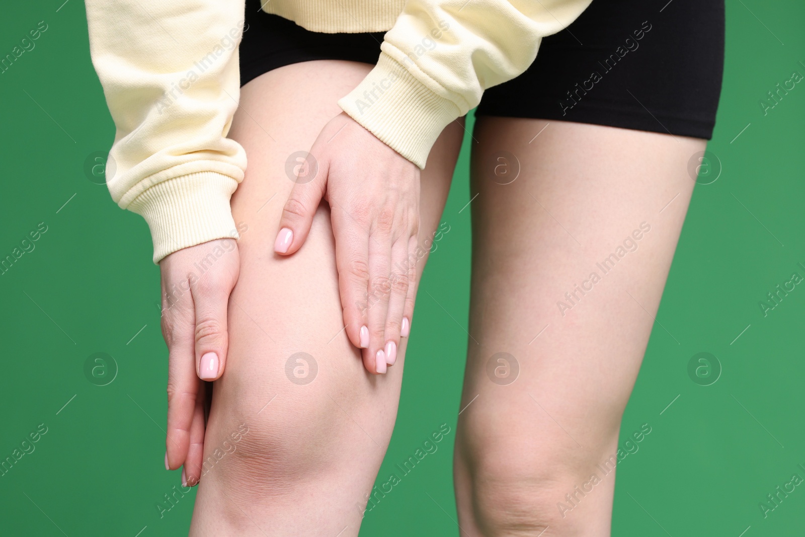 Photo of Young woman suffering from pain in knee on green background, closeup