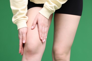 Young woman suffering from pain in knee on green background, closeup