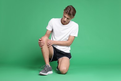 Photo of Young man suffering from pain in knee on green background