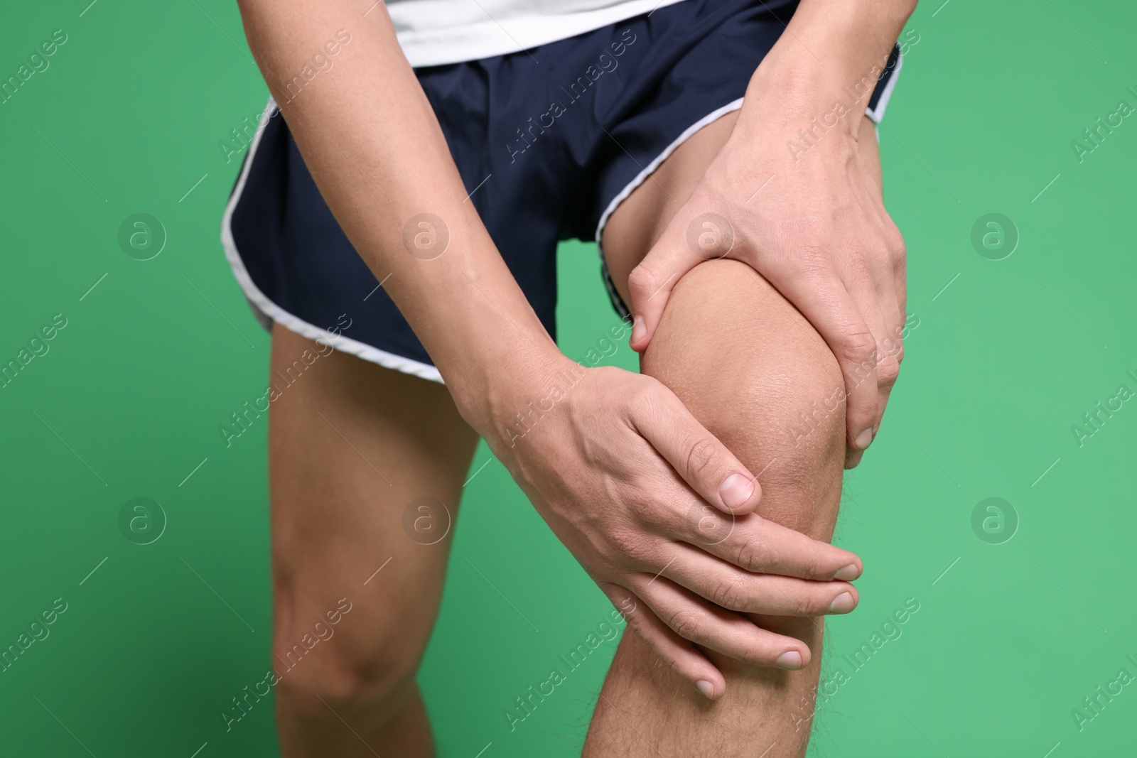 Photo of Young man suffering from pain in knee on green background, closeup