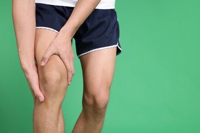 Photo of Young man suffering from pain in knee on green background, closeup. Space for text