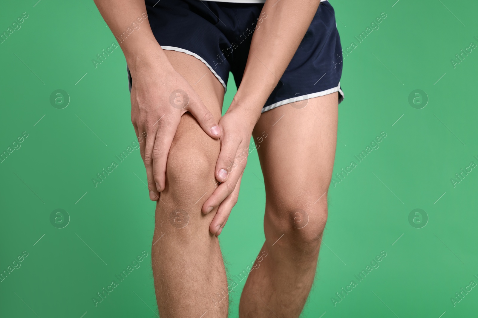 Photo of Young man suffering from pain in knee on green background, closeup