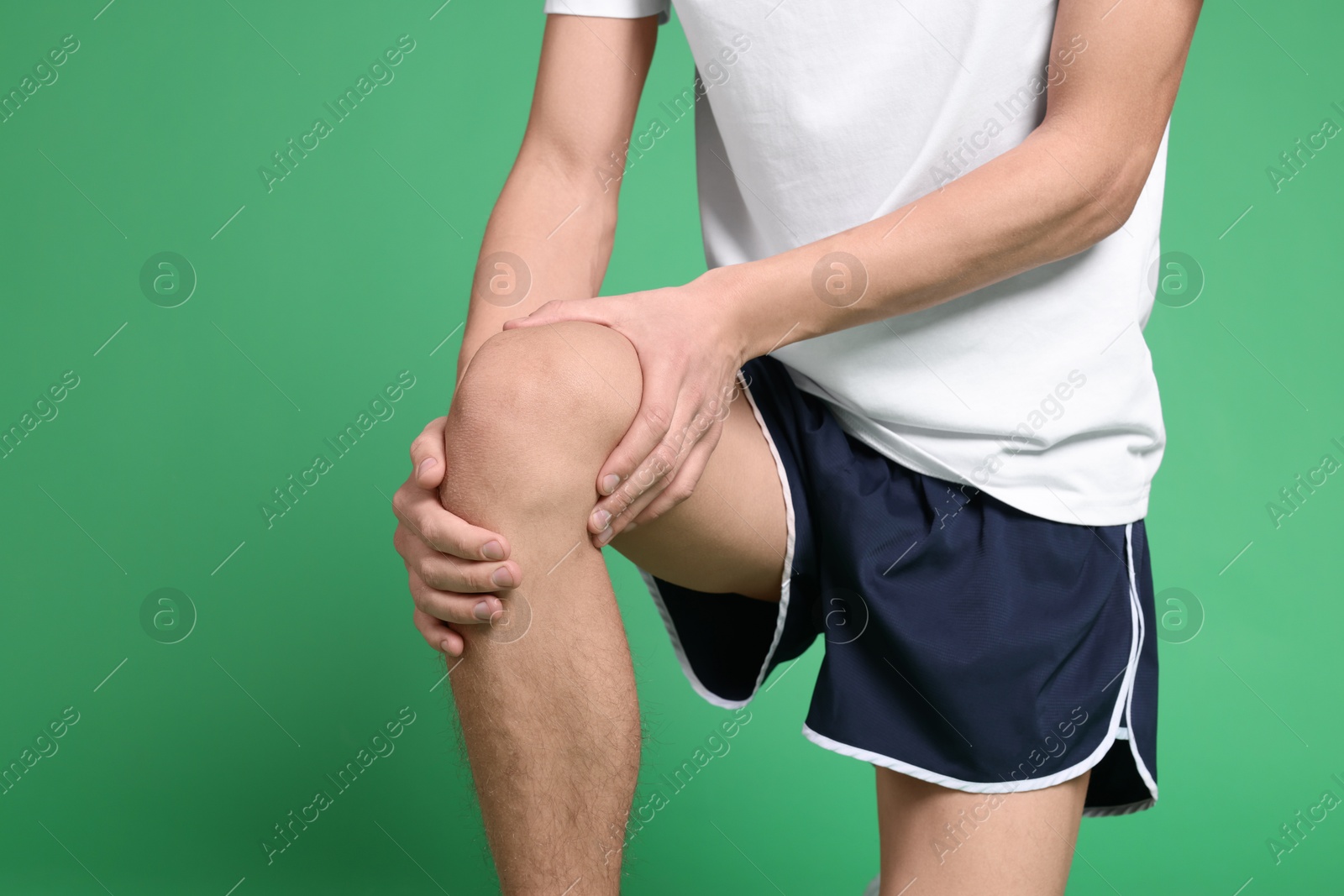 Photo of Young man suffering from pain in knee on green background, closeup