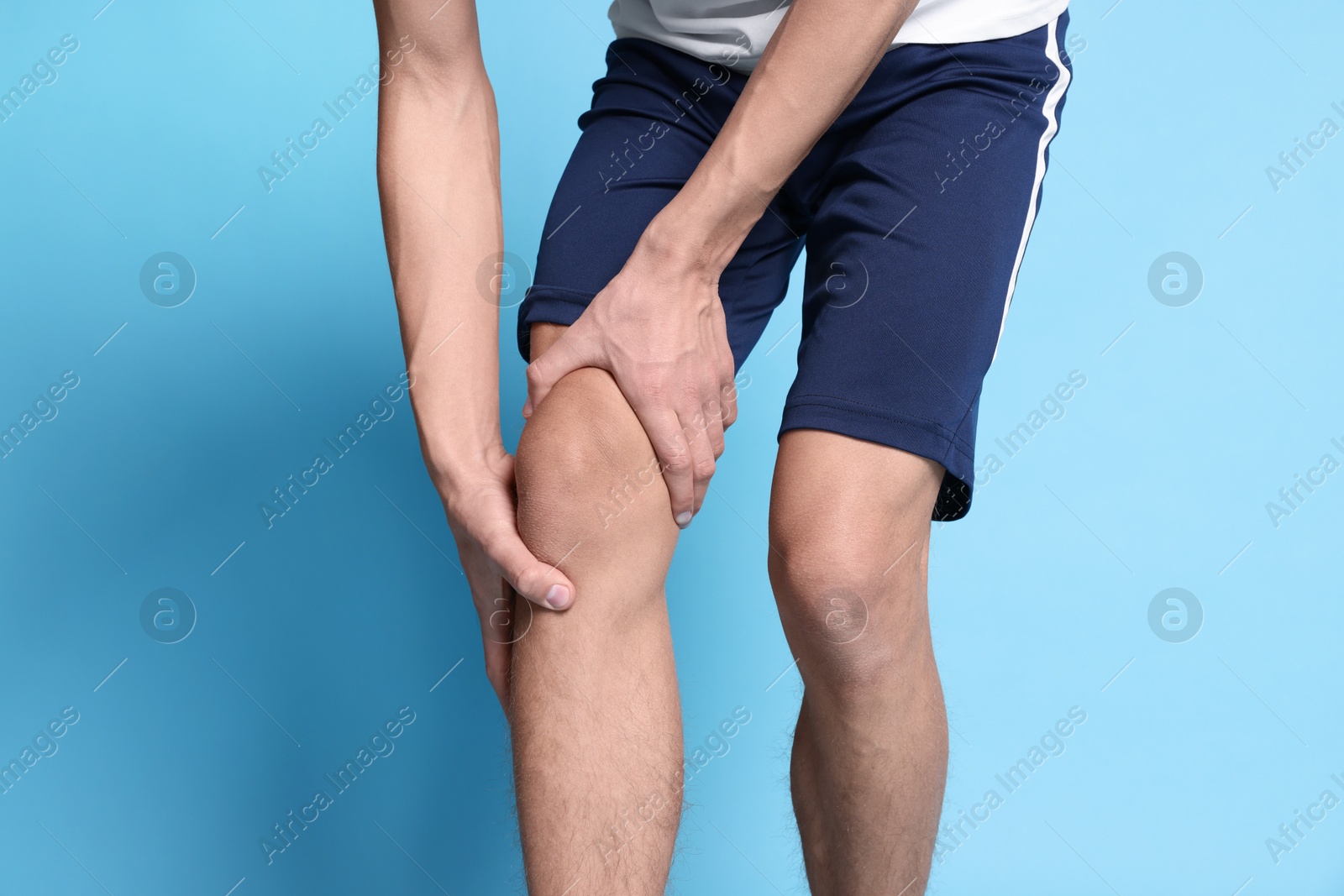 Photo of Young man suffering from pain in knee on light blue background, closeup