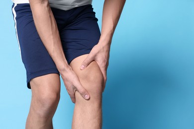 Photo of Young man suffering from pain in knee on light blue background, closeup. Space for text