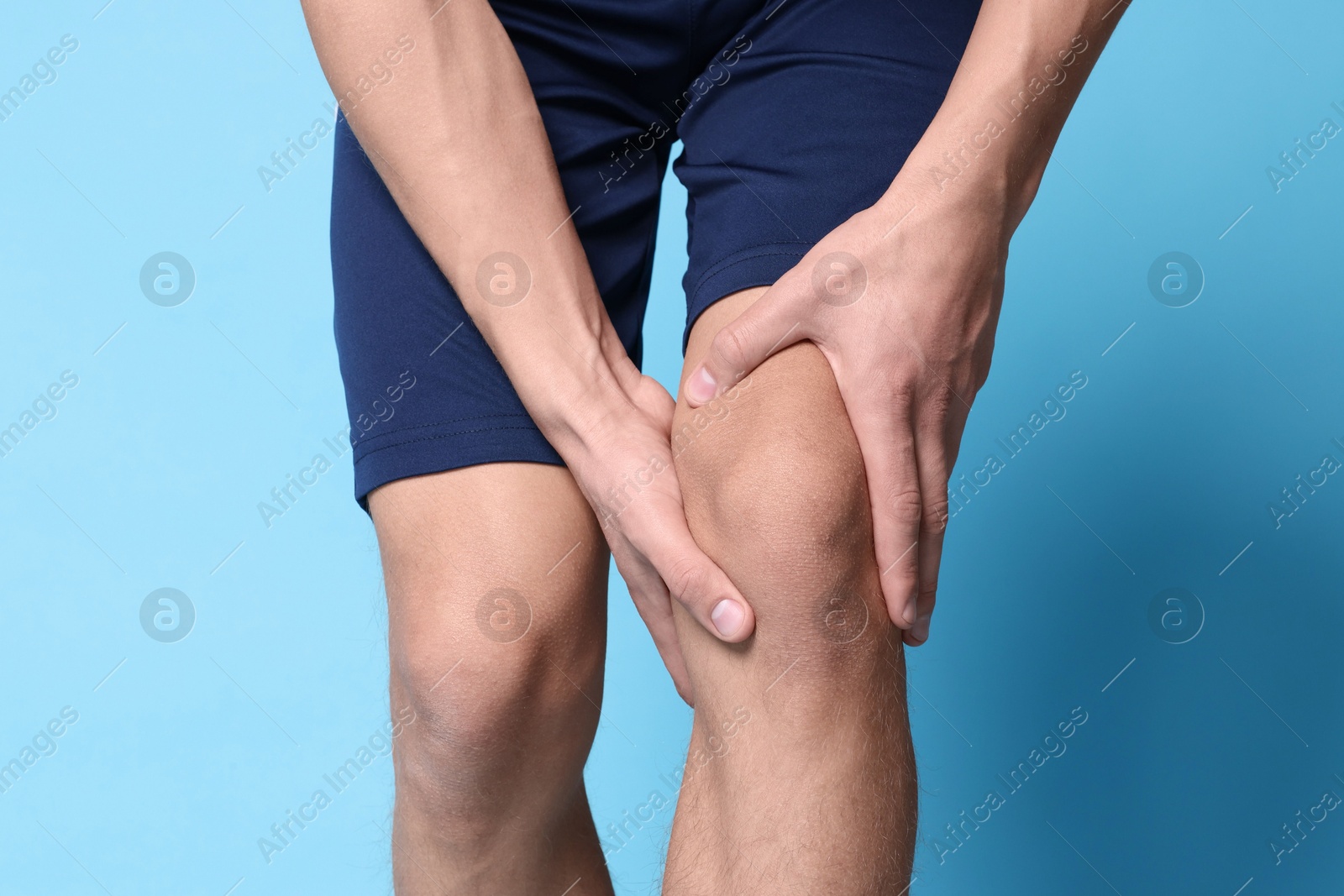 Photo of Young man suffering from pain in knee on light blue background, closeup