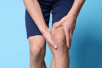 Photo of Young man suffering from pain in knee on light blue background, closeup