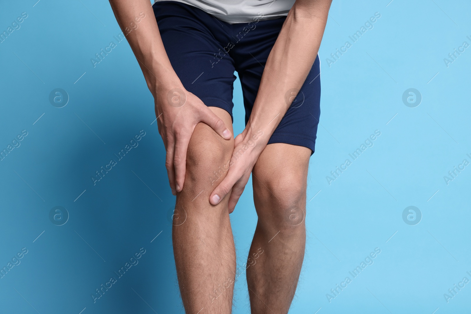 Photo of Young man suffering from pain in knee on light blue background, closeup