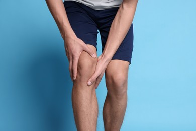 Young man suffering from pain in knee on light blue background, closeup