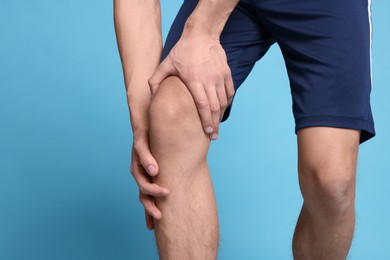 Young man suffering from pain in knee on light blue background, closeup