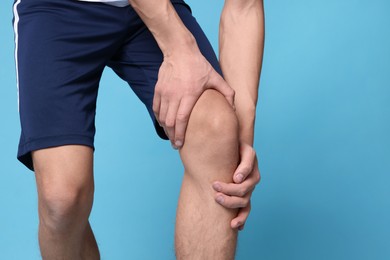 Young man suffering from pain in knee on light blue background, closeup