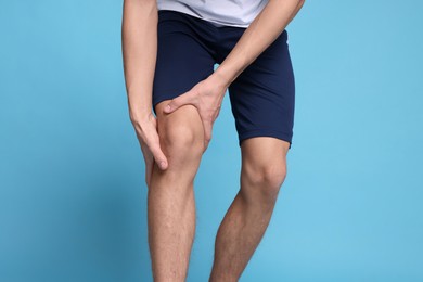 Photo of Young man suffering from pain in knee on light blue background, closeup