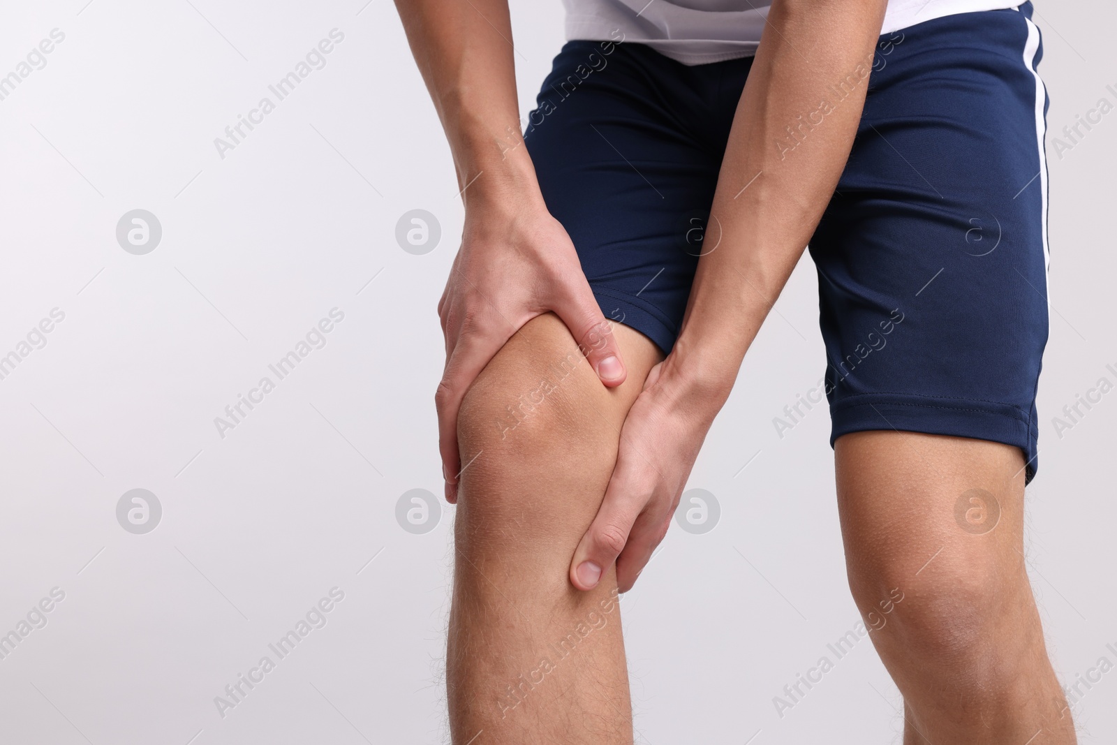 Photo of Young man suffering from pain in knee on light grey background, closeup