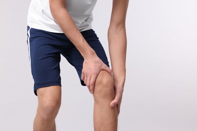 Young man suffering from pain in knee on light grey background, closeup